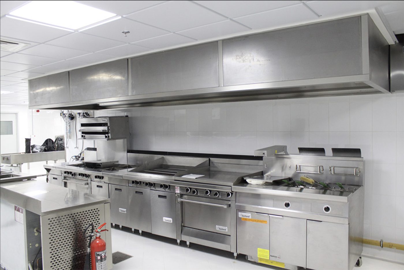 Commercial kitchen cooking line with ranges, griddle and fryers under a stainless steel extraction canopy