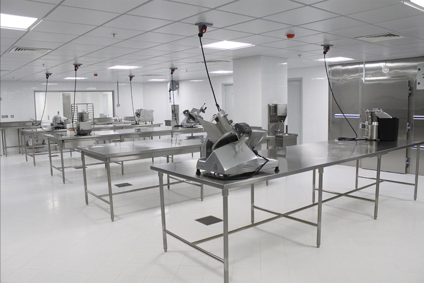 Food preparation hall with stainless steel work tables, meat slicers and a cold room door